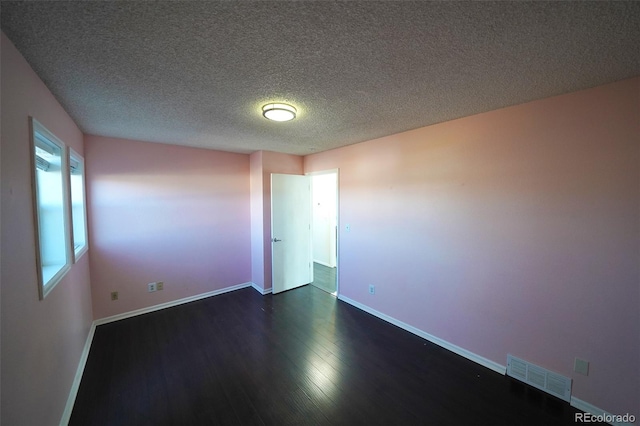 spare room with a textured ceiling and dark hardwood / wood-style flooring