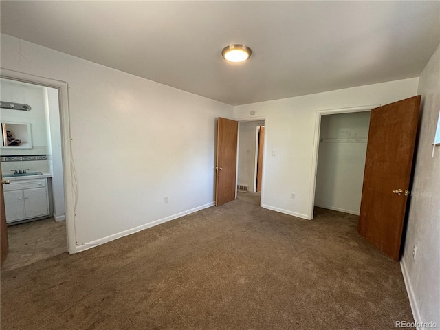 unfurnished bedroom with sink, dark carpet, and a closet