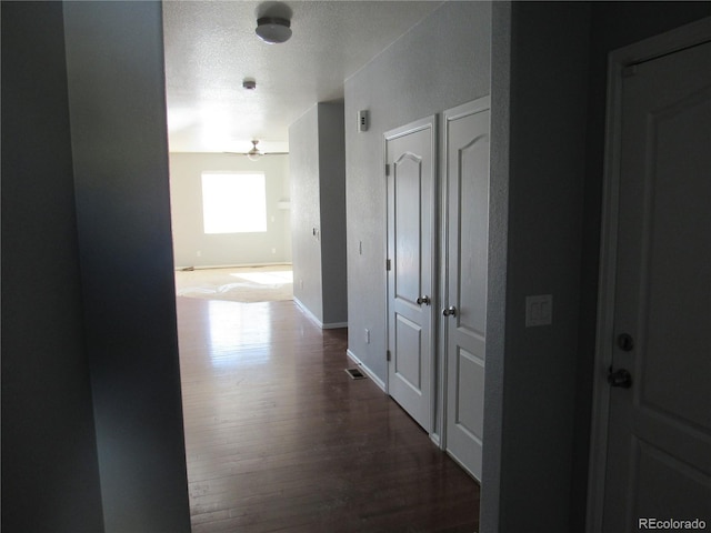 hallway with a textured ceiling, baseboards, and wood finished floors