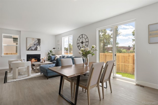 dining room with baseboards, visible vents, wood finished floors, and a glass covered fireplace