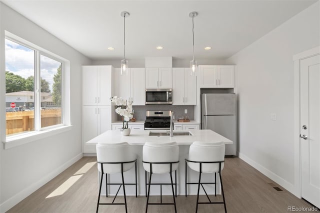 kitchen featuring white cabinets, a center island with sink, backsplash, and appliances with stainless steel finishes