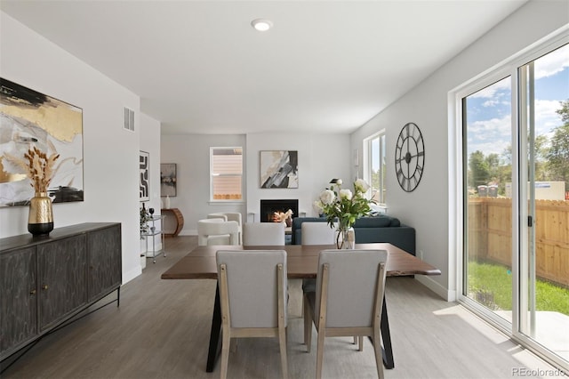 dining space with a warm lit fireplace, baseboards, visible vents, and wood finished floors