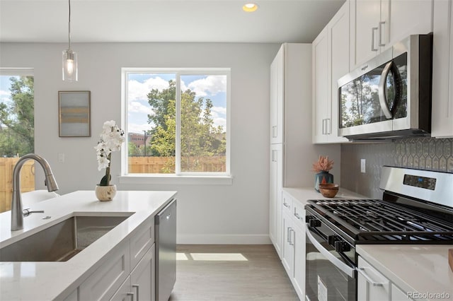 kitchen featuring decorative backsplash, a sink, light stone counters, pendant lighting, and appliances with stainless steel finishes