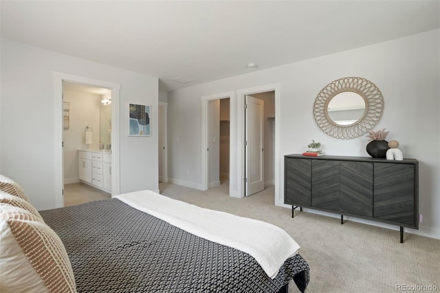 bedroom with ensuite bathroom, baseboards, a spacious closet, and light carpet