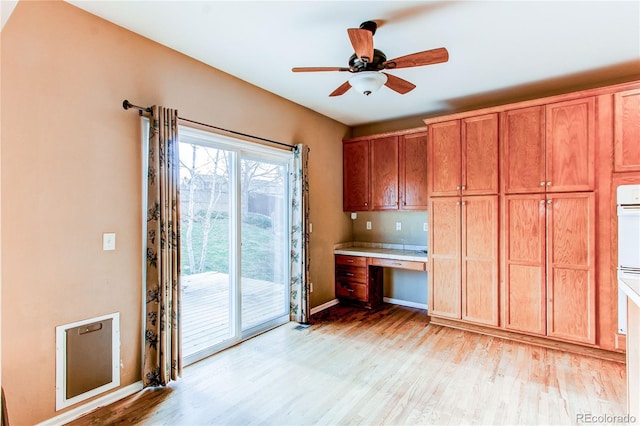 kitchen featuring baseboards, light wood-type flooring, a ceiling fan, brown cabinets, and built in study area