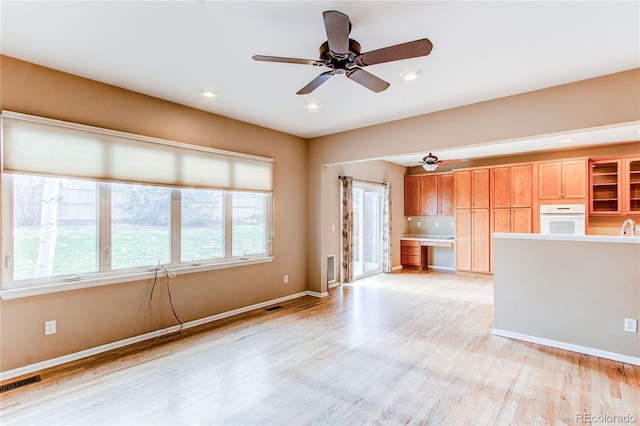 unfurnished living room with visible vents, light wood-type flooring, a ceiling fan, and baseboards