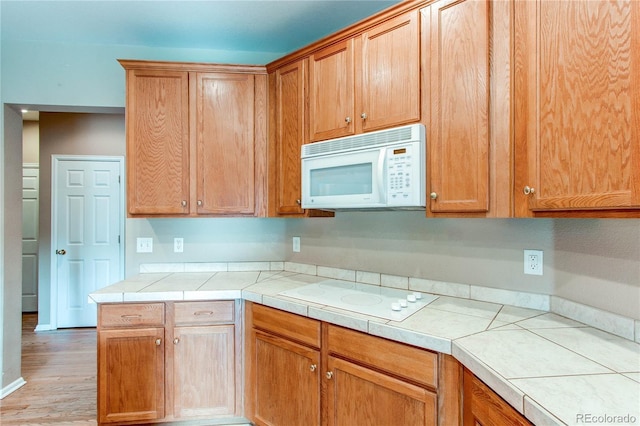 kitchen featuring white appliances, light wood-type flooring, and tile counters
