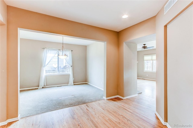 empty room featuring visible vents, baseboards, wood finished floors, and ceiling fan with notable chandelier