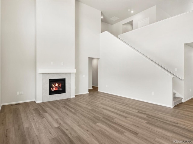 1612 Colorado River Dr, Windsor, CO 80550 - unfurnished living room with stairway, wood finished floors, a tiled fireplace, a high ceiling, and recessed lighting
