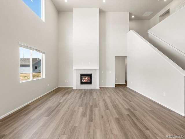 1612 Colorado River Dr, Windsor, CO 80550 - unfurnished living room with a towering ceiling, wood finished floors, a tile fireplace, stairs, and recessed lighting