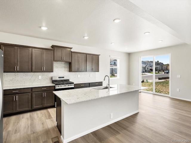 1612 Colorado River Dr, Windsor, CO 80550 - kitchen with light wood finished floors, dark brown cabinetry, decorative backsplash, a center island with sink, and stainless steel gas range oven