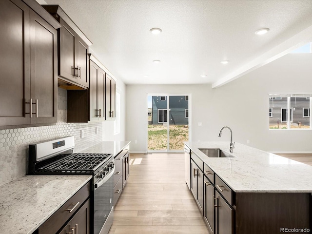 1612 Colorado River Dr, Windsor, CO 80550 - kitchen featuring stainless steel range with gas stovetop, light wood-type flooring, dark brown cabinets, a kitchen island with sink, and decorative backsplash