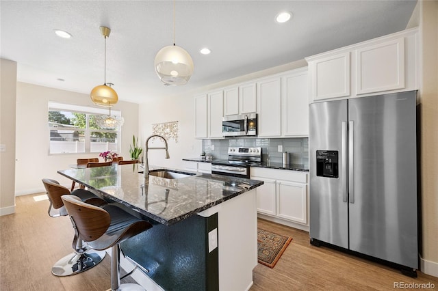 4177 E 98th Pl, Thornton, CO 80229 - kitchen with stainless steel appliances, light wood-type flooring, an island with sink, white cabinetry, and tasteful backsplash