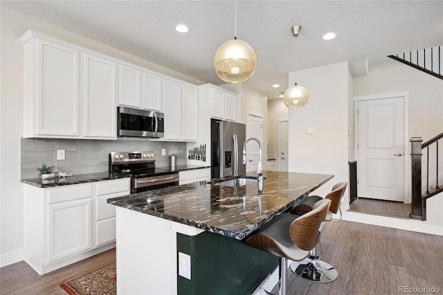 4177 E 98th Pl, Thornton, CO 80229 - kitchen featuring appliances with stainless steel finishes, wood finished floors, a center island with sink, decorative backsplash, and white cabinets