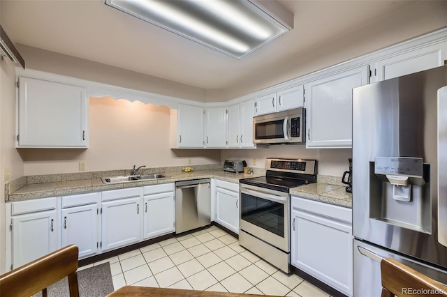 kitchen featuring tile countertops, light tile patterned floors, a sink, white cabinets, and appliances with stainless steel finishes