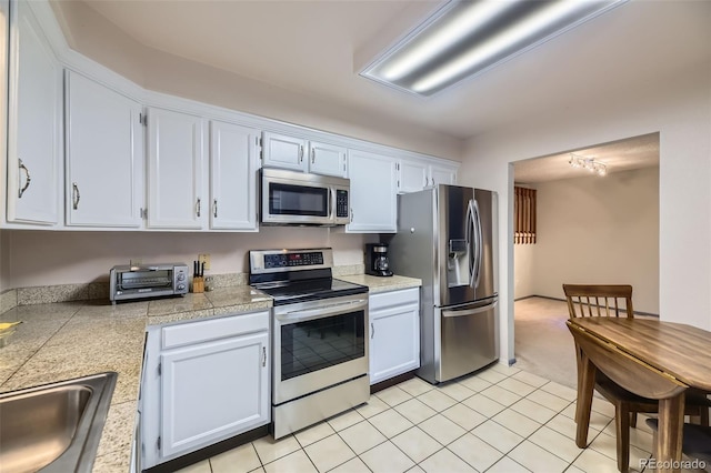 kitchen with a toaster, light tile patterned floors, stainless steel appliances, tile counters, and a sink