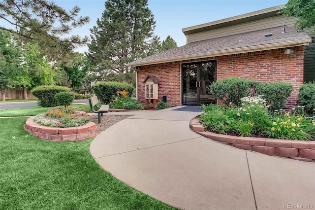 exterior space featuring roof with shingles, brick siding, a lawn, and french doors