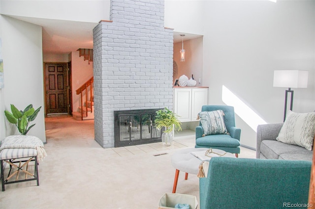 carpeted living area with a brick fireplace, a high ceiling, and stairway