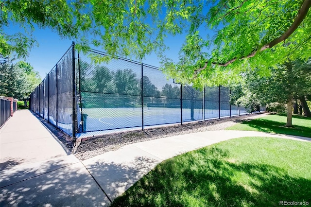 view of basketball court featuring a yard, a tennis court, and fence