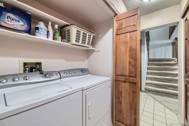 laundry area with light tile patterned floors, laundry area, washing machine and dryer, and a textured ceiling