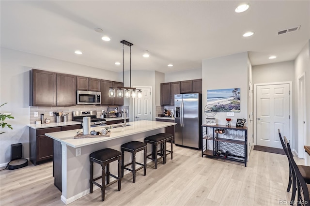 kitchen with decorative backsplash, appliances with stainless steel finishes, decorative light fixtures, and dark brown cabinets