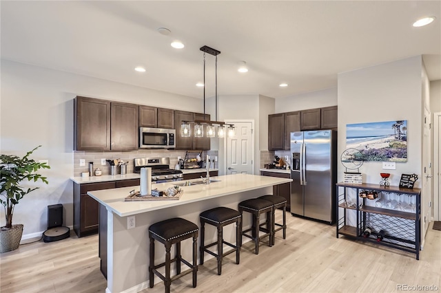 kitchen with appliances with stainless steel finishes, backsplash, dark brown cabinetry, sink, and decorative light fixtures