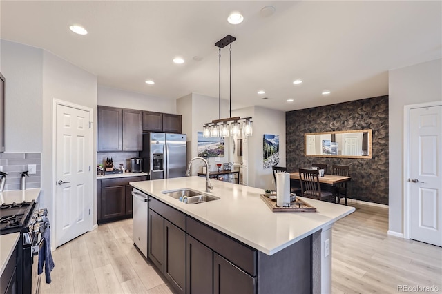 kitchen with sink, stainless steel appliances, decorative light fixtures, a kitchen island with sink, and dark brown cabinets