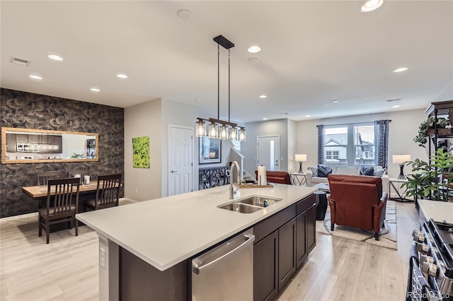 kitchen with a center island with sink, sink, appliances with stainless steel finishes, decorative light fixtures, and light hardwood / wood-style floors