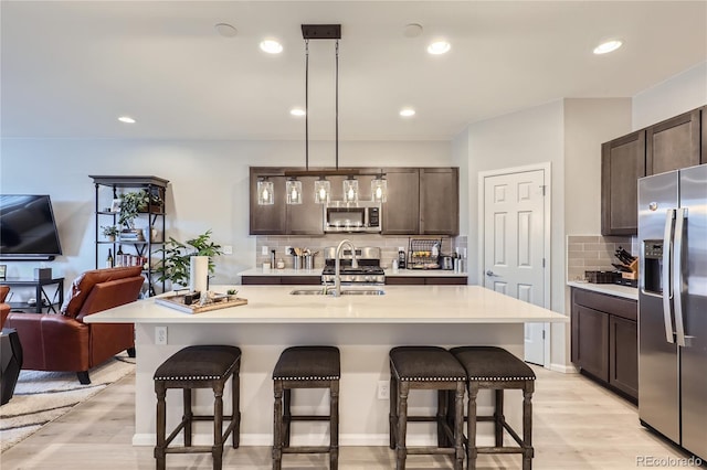 kitchen with decorative light fixtures, dark brown cabinetry, stainless steel appliances, and a kitchen island with sink