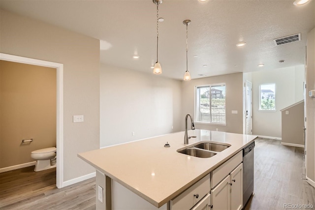 kitchen featuring sink, decorative light fixtures, white cabinetry, an island with sink, and stainless steel dishwasher