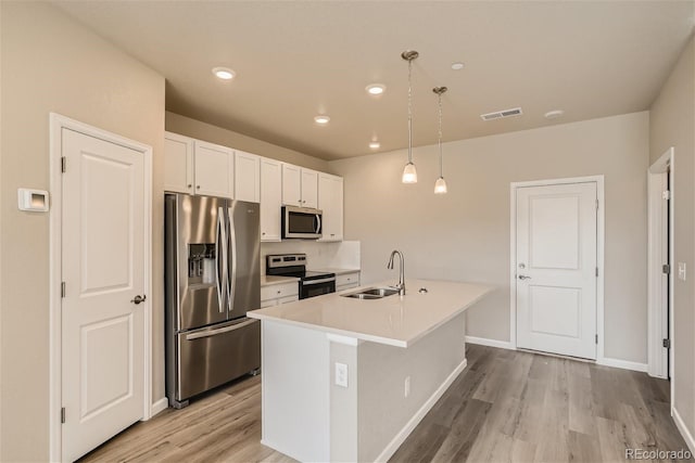 kitchen featuring decorative light fixtures, stainless steel appliances, a kitchen island with sink, white cabinetry, and sink