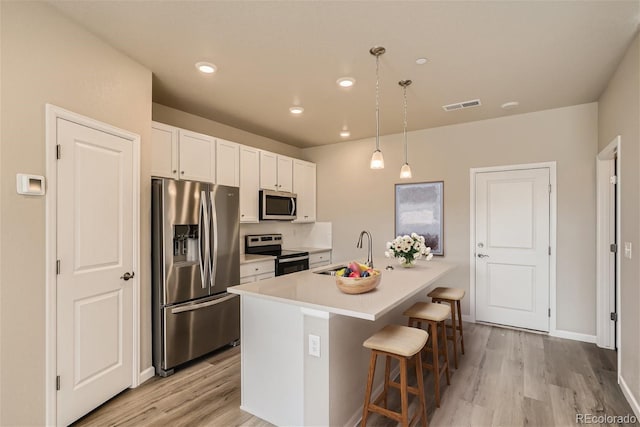 kitchen featuring stainless steel appliances, sink, a breakfast bar area, hanging light fixtures, and a center island with sink