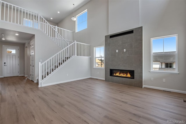 3394 N Grand Baker Ct, Aurora, CO 80019 - unfurnished living room with a towering ceiling, stairway, wood finished floors, a tile fireplace, and recessed lighting