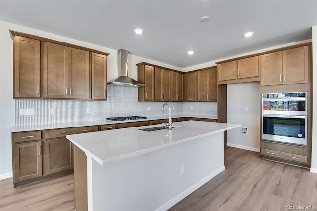3394 N Grand Baker Ct, Aurora, CO 80019 - kitchen featuring wall chimney exhaust hood, light wood-type flooring, appliances with stainless steel finishes, decorative backsplash, and a kitchen island with sink