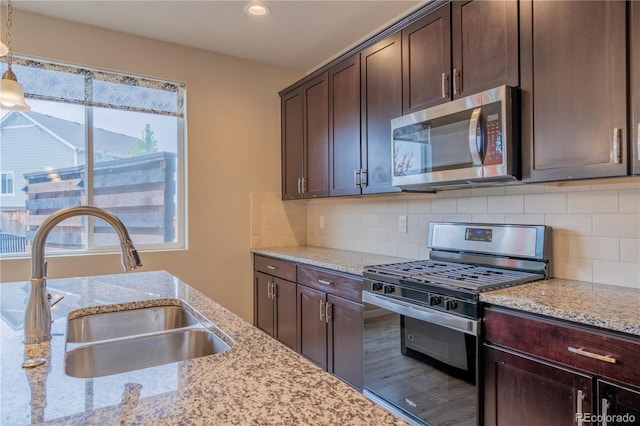 kitchen with hanging light fixtures, a sink, dark brown cabinetry, light stone countertops, and appliances with stainless steel finishes