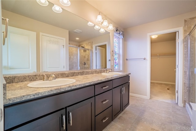 bathroom with a walk in closet, double vanity, a stall shower, and a sink