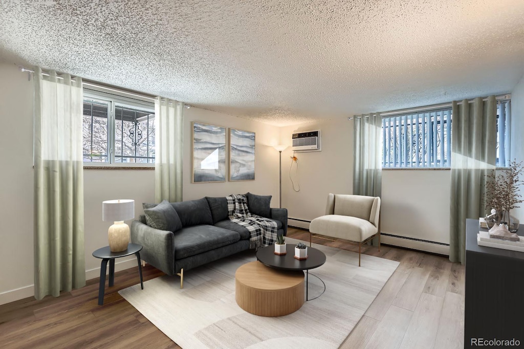 living area with a wall mounted AC, a textured ceiling, wood finished floors, and a baseboard heating unit