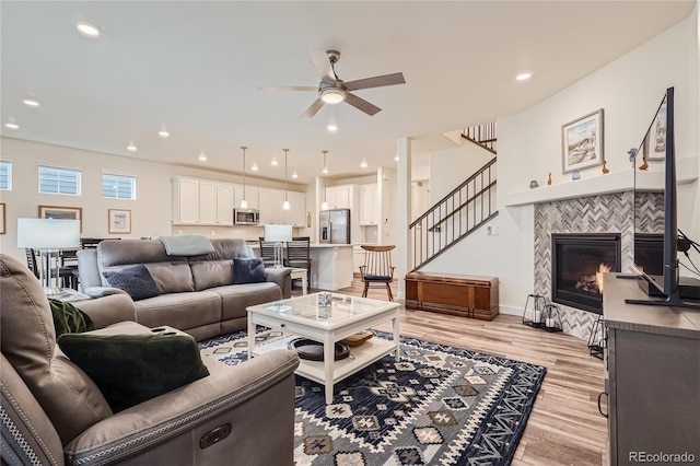 living room featuring ceiling fan, recessed lighting, stairway, light wood-style flooring, and a tile fireplace