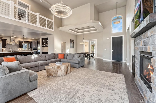 living room featuring dark hardwood / wood-style flooring, a stone fireplace, a high ceiling, and an inviting chandelier