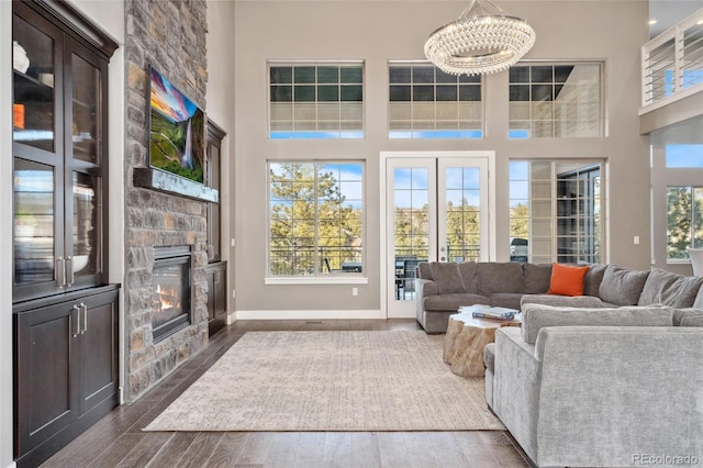 living room with a high ceiling, a stone fireplace, a chandelier, and dark hardwood / wood-style flooring