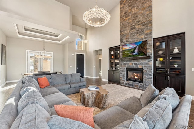 living room with a stone fireplace, a tray ceiling, a notable chandelier, hardwood / wood-style floors, and a high ceiling