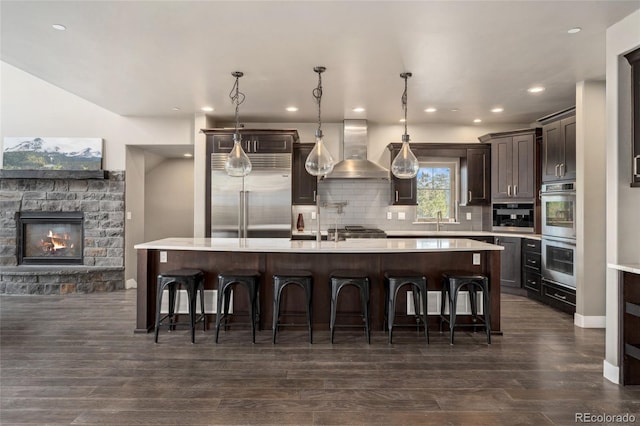 kitchen with a spacious island, appliances with stainless steel finishes, wall chimney exhaust hood, and decorative light fixtures