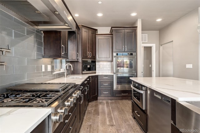 kitchen featuring sink, hardwood / wood-style flooring, appliances with stainless steel finishes, light stone countertops, and wall chimney exhaust hood