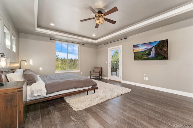 bedroom with dark wood-type flooring, ceiling fan, a tray ceiling, and access to outside