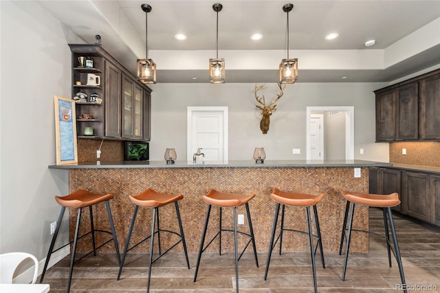 kitchen with dark brown cabinetry, a kitchen bar, kitchen peninsula, and backsplash