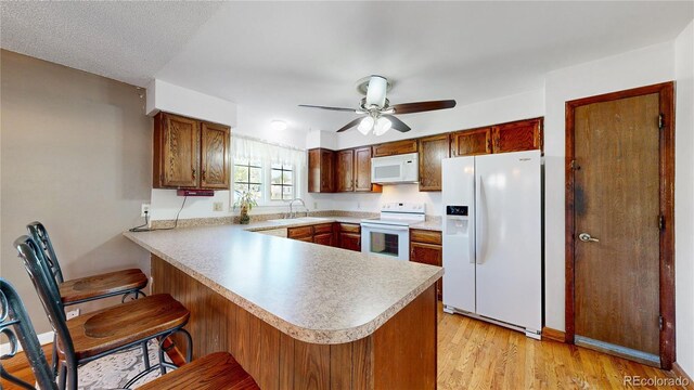 kitchen featuring white appliances, light hardwood / wood-style floors, kitchen peninsula, sink, and ceiling fan