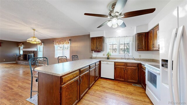 kitchen with white appliances, a fireplace, kitchen peninsula, sink, and ceiling fan