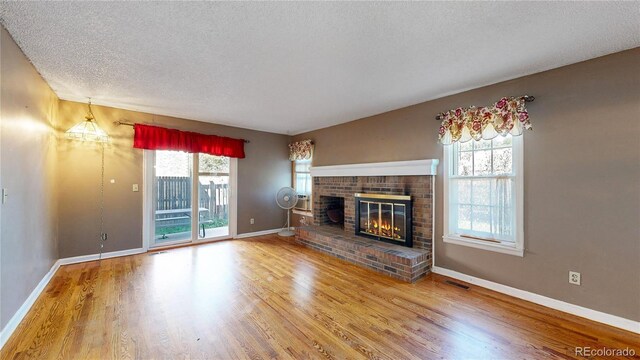 unfurnished living room featuring a textured ceiling, wood-type flooring, and a brick fireplace