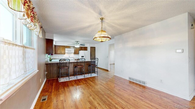 kitchen with light wood-type flooring, white appliances, ceiling fan, kitchen peninsula, and a breakfast bar area