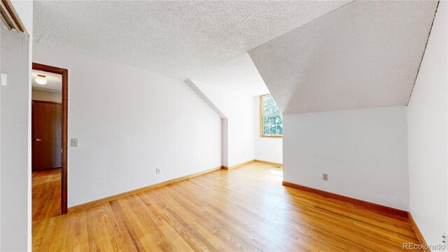 additional living space with lofted ceiling, light hardwood / wood-style flooring, and a textured ceiling